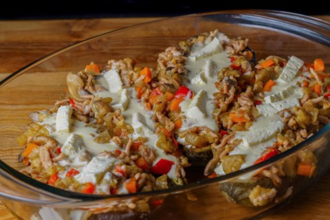 Eggplants stuffed with meat and vegetables covered with bechamel sauce on a glass tray on a wooden table