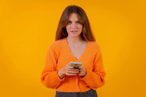 A woman looking at things on the internet on the mobile phone on a yellow background