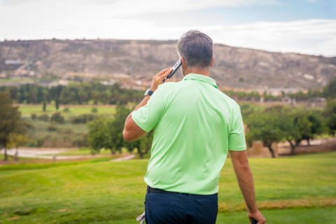 Young businessman playing golf and answering a work call with the phone from the club