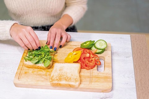 Unrecognizable person cooking a vegetable sandwich in the kitchen at home. Placing the arugula