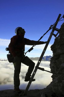 Silhouette of mountain climber climbing metal ladder of Via ferrata in the Swiss Alps