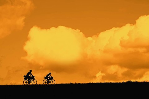 Couple of young cyclists riding their touring bicycles silhouetted against orange sunset sky in summer