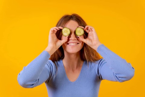 Vegan woman with cucumber slices on her eyes on a yellow background