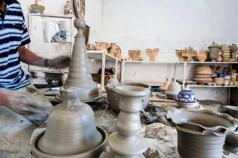 Skillful potter forming a vessel out of gray clay in a pottery factory