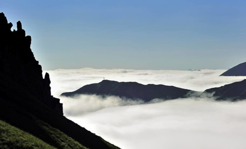 View over silhouetted jagged mountain edge and mountains covered in mist at sunrise seen from the Col du Tourmalet