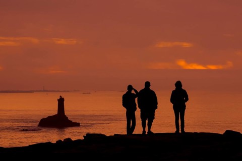 Tourists watching the lighthouse La Vieille in the strait Raz de Sein silhouetted against sunset at the Pointe du Raz