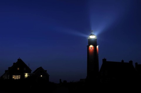Houses and light beams from lantern of the Cocksdorp lighthouse Eierland at night