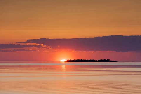 Sunset with sun setting behind silhouetted island in Lake Vaenern
