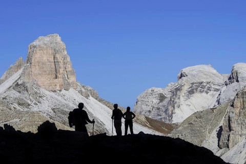 Three mountain walkers silhouetted against Torre dei Scarperi