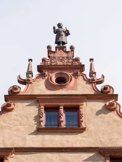 The top of a medieval building La Maison des Tetes with a male statue at the top of Rue des Tetes