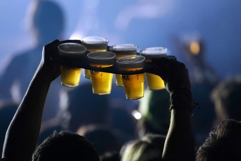 Ambiance during live rock concert and man bringing beer in plastic cups to friends among spectators