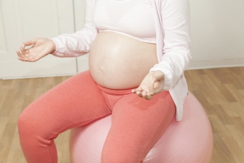 Pregnant woman sitting on an exercise ball and meditating