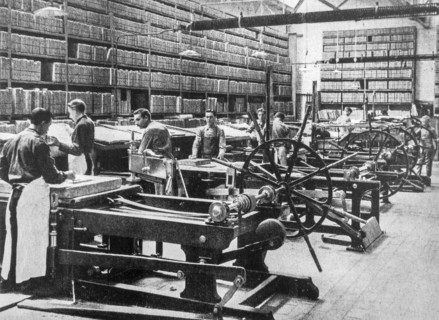 1890s black and white archival photo showing pressmen working on lithographic printing presses and racks for storing lithography stones in pressroom