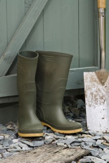 Pair of green wellington boots and a spade outside a garden shed