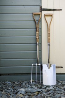 Garden fork and spade leaning against a painted shed