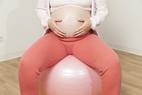 Pregnant woman sitting on exercise ball with hands on baby belly | MR:yes NH_pregnant_belly_mr