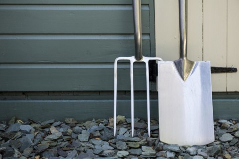 Garden fork and spade leaning against a painted shed
