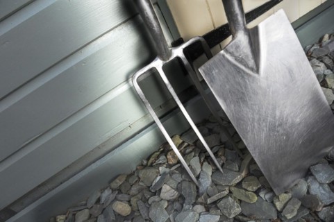 Garden fork and spade leaning against a painted shed