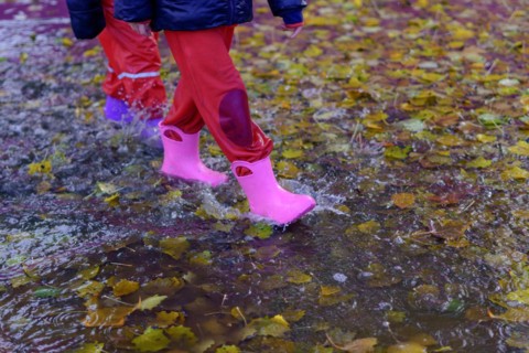 Two children walking through a puddle of water with their boots on a rainy day