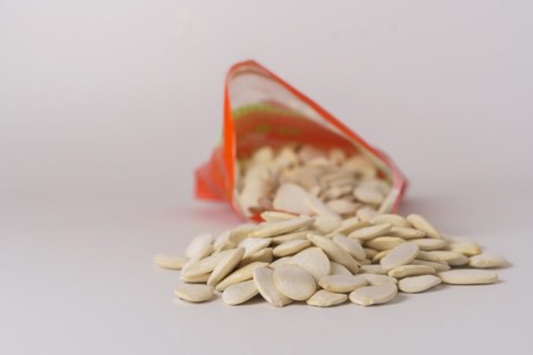 Roasted pumpkin seeds with salt coming out of their red bag on a white table with copy space