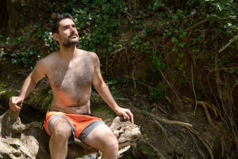 Man in swimsuit sitting on a tree trunk on a river bank