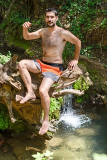 Man in swimsuit sitting on a tree trunk on a river bank
