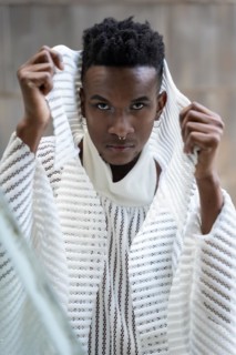 A young man of African ethnicity in a white contemporary suit and black leather boots