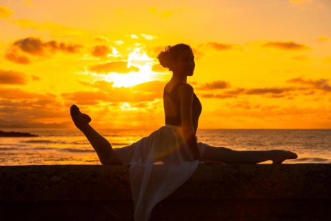 Silhouette of a young woman dancer next to the beach at sunset doing spagata with the sea in the background