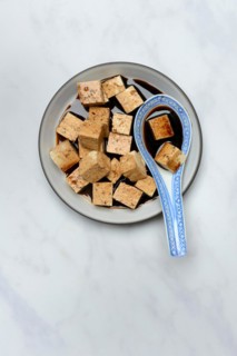 Soy sauce marinated tofu cubes in bowl with Asian ceramic spoon