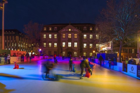 Skaters on a colourfully illuminated artificial ice rink