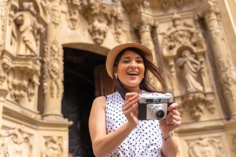Tourist woman smiling with hat visiting a church and taking photos with a camera