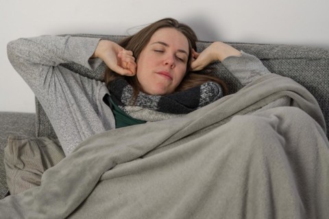 Woman waking up from a nap on the couch at home covered with a blanket and scarf