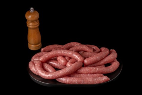 Homemade meat sausages with pepper shaker isolated on black background and copy space