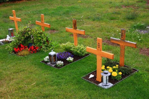 Flower decorated anonymous urn graves with wooden cross with inscription Here rests in God