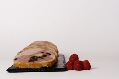 Close-up of a chicken stuffed with raspberry and goat cheese with a bowl of raspberry sauce isolated on white background