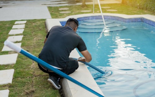 Maintenance person cleaning swimming pool with suction hose