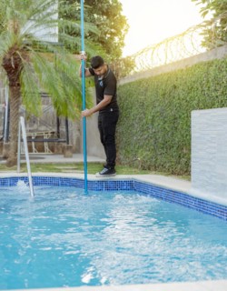 Young man cleaning a swimming pool with a vacuum hose