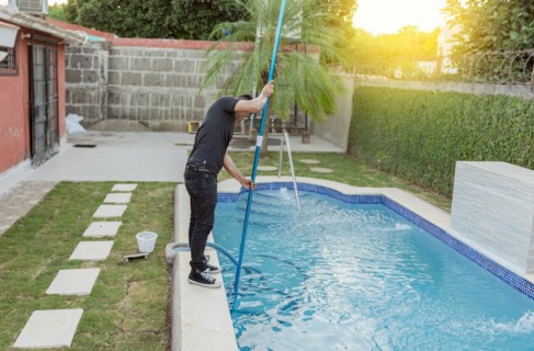 Man cleaning and maintaining swimming pools with a suction hose