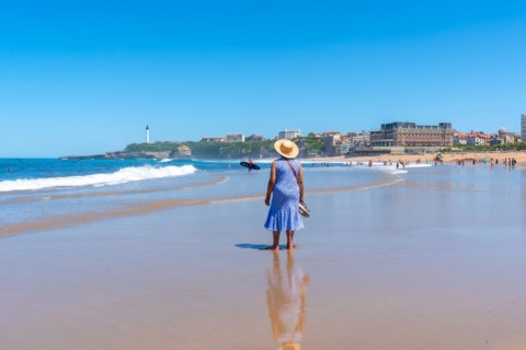 An elderly woman with a hat walking on the beach in Biarritz