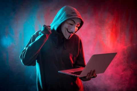 Hacker with an anonymous mask with a computer and making a fight symbol