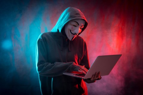 Hacker with anonymous mask with a computer and with a background of smoke and colored led