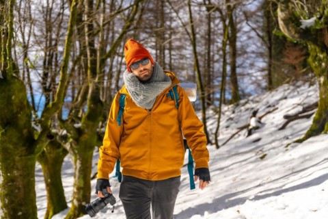 Portrait of a photographer trekking with a backpack taking photos in a beech forest with snow