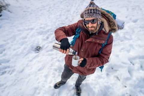Portrait of man having breakfast a hot coffee from a thermos in winter in the snow before starting the trekking