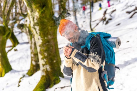 A man smoking lighting a cigarette with a lighter on a snowy mountain in winter