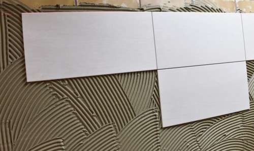 Tiler has applied tile adhesive and is sticking on new tiles
