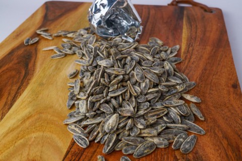 Roasted sunflower seeds with salt coming out of their bag on white background and copy space