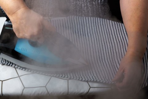 Woman ironing a striped T-shirt by steaming the iron