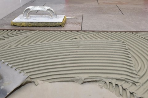 Tiler has applied tile adhesive to floor