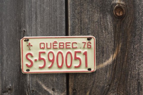 Vintage 1976 Quebec province license plate displayed on side wall of wood plank storage shed