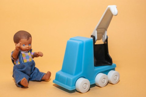 A car crane and a little dolls boy set against a beige background